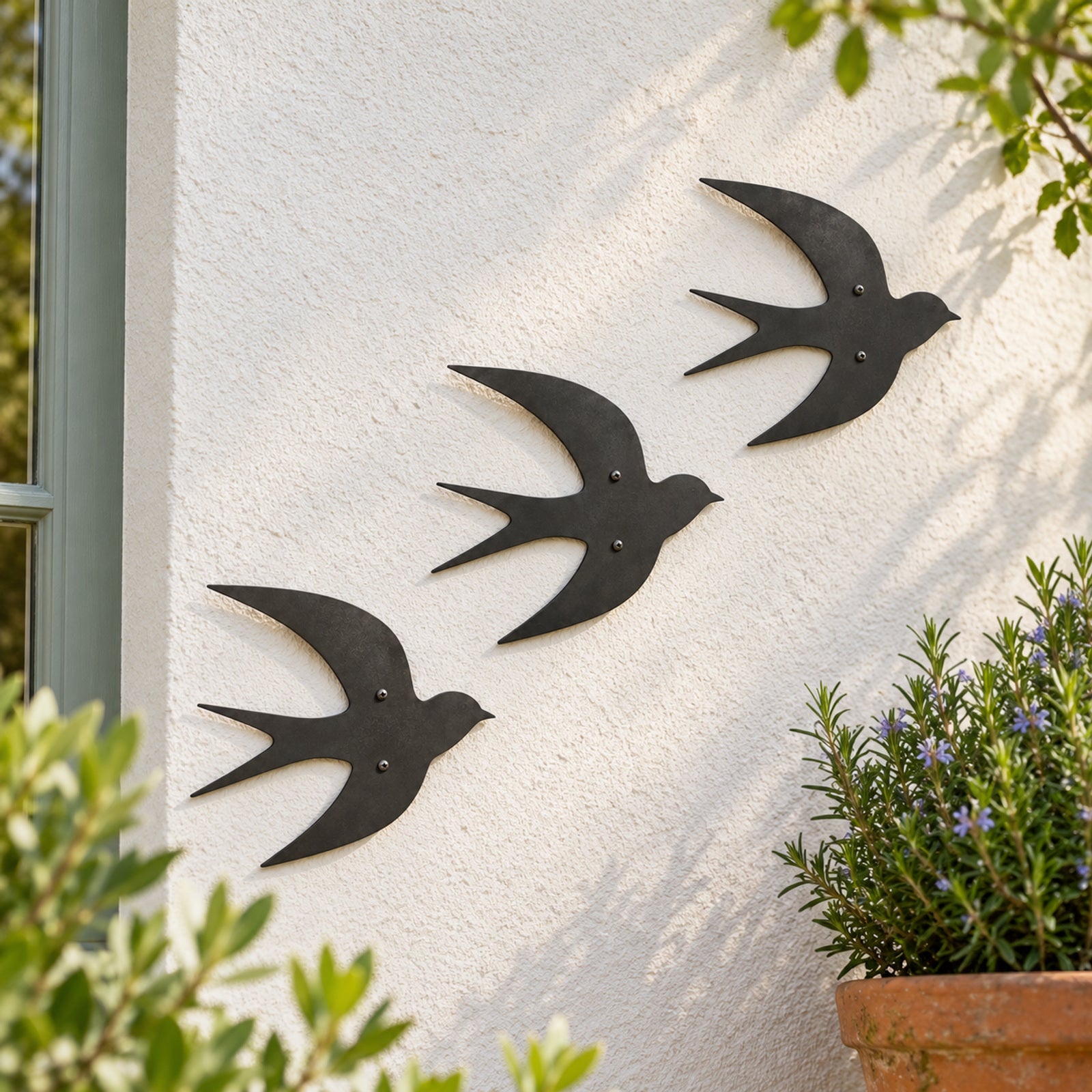 Three charcoal swallow silhouettes on a garden wall